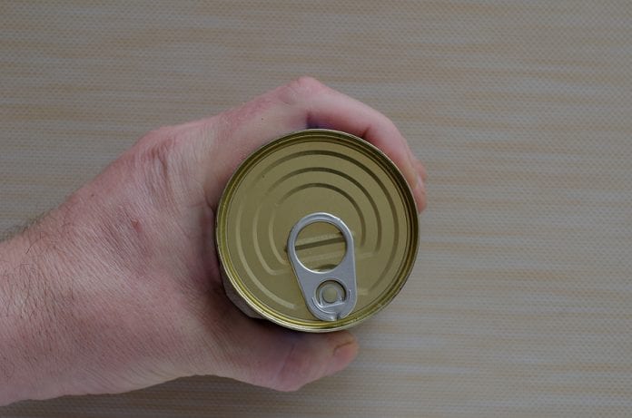 Hand Of An Adult Man Holds A Can Of Canned Food. Closed Tin Can
