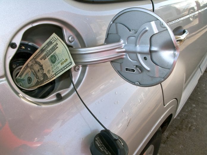 Money sticking out of automobile fuel tank opening signifying an
